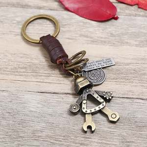 Vintage robot keychain with woven leather strap and bronze metal pendant on wood surface