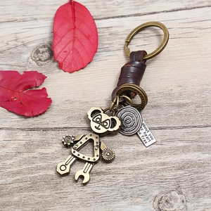 Retro mechanical robot keychain with brown braided leather strap on a rustic wood surface