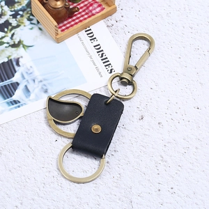 Retro bronze alloy keychain with black leather strap and vintage bird charm on white texture
