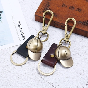 Vintage bronze baseball cap keychain with black and brown leather straps on a wooden base