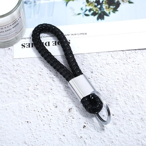 Detail of hand-woven black leather keychain with polished silver metal ring on white stone