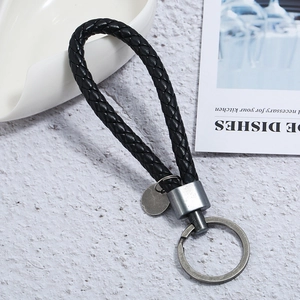 Close-up of hand-woven black leather keychain with vintage silver ring on marble surface