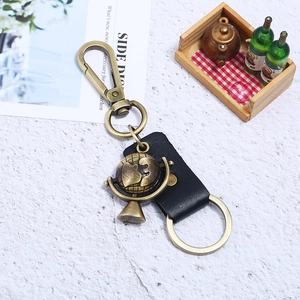 Vintage bronze globe keychain with black leather strap and lobster clasp on a white surface