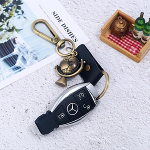 Vintage globe keychain with black leather strap and brass metal clip on a white surface