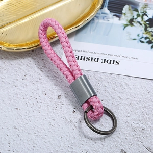 Close-up of pink woven leather keychain with matte grey metal ring on a textured surface