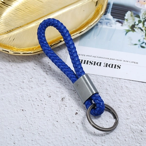 Close-up of blue braided leather keychain with gun-black metal clasp on white texture