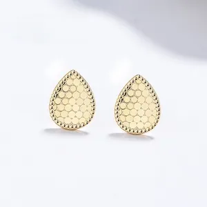 Close-up of golden teardrop earrings with honeycomb texture and beaded border detail