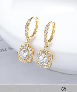 Detail of square gold drop earrings with sparkling zircon stones on a white ceramic rim