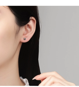 Close-up of minimalist silver round bead stud earring worn on a model's earlobe