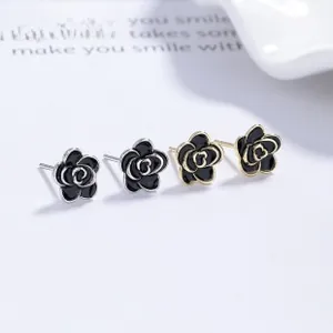 Detail of silver and gold camellia flower earrings with black enamel on a card