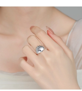 Detail of shell-shaped silver ring on finger showing fan textures and metallic luster