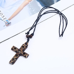 Vintage resin cross pendant necklace with black braided cord and wood beads on white desk