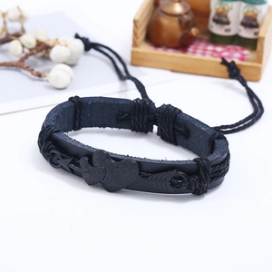 Macro detail of black braided leather bracelet featuring a metallic heart-and-arrow charm