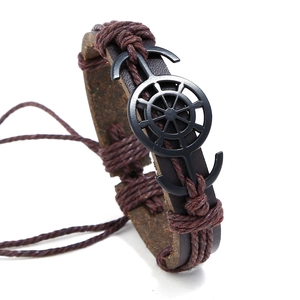 Close-up of vintage braided leather bracelet featuring nautical anchor and helm charms