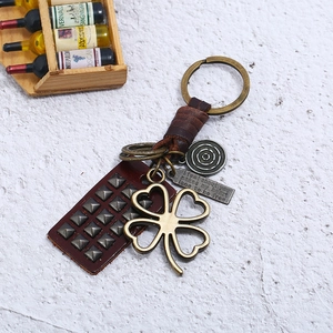 Vintage woven leather keychain with clover charm and engraved metal tags on stone surface