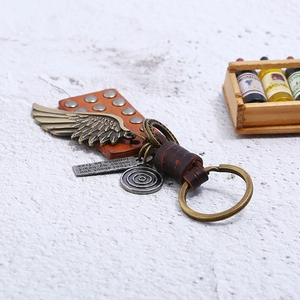 Vintage punk leather keychain with metal wings and motivational plaque on marble surface