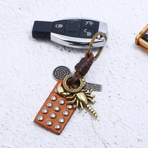 Retro handmade leather keychain with bronze scorpion pendant and metal studs on white wood