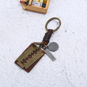 Punk woven leather keychain with vintage bronze razor blade and metal tags on stone background