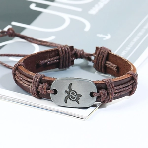 Dettaglio di un bracciale in pelle marrone con placca in metallo tartaruga e pace