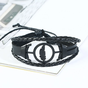 Detail view of multi-layer black leather bracelet with a metallic feather charm and woven cords