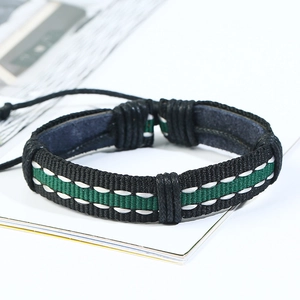 Macro detail of braided black and green leather bracelet with woven stitching on white book