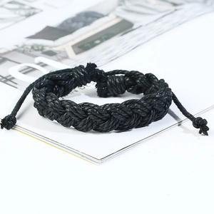 Détail d'un bracelet en cuir tressé noir avec cordons réglables posé sur un magazine de mode