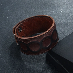 Détail d'un large bracelet punk en cuir marron avec motifs en relief et bouton pression métal