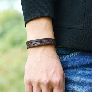 Minimalist dark brown leather bracelet with red stitching shown on a male wrist outdoors
