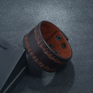 Close-up of wide brown leather cuff bracelet featuring snap buttons and woven stitching