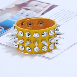 Detail of punk yellow leather bracelet with three rows of silver metal spikes on a magazine