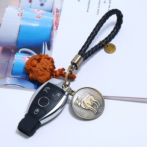 Detail of leather braid keychain with carved wood Pixiu and bronze Aries zodiac pendant