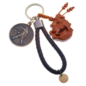 Close-up of Libra zodiac metal tag and carved wooden pendant on woven leather keychain