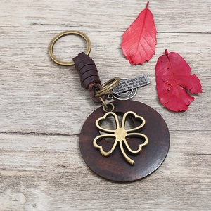 Vintage braided leather keychain with wooden disc and clover pendant on wood background