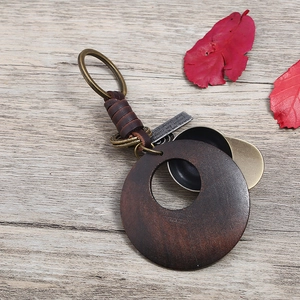 Vintage braided leather keychain with wooden pendant and metal hat charm on wood background