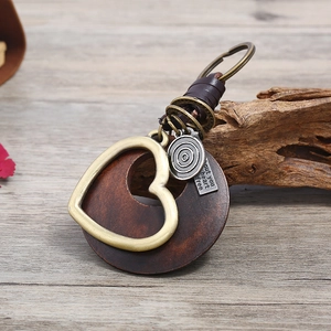 Retro leather keychain featuring round wood disk and brass heart pendant on a wooden table