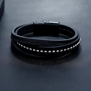Détail d'un bracelet multicouche en cuir noir avec clous argentés et fermoir magnétique