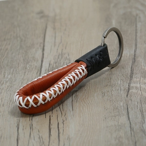Handmade brown leather keychain with white cross-stitching and metal ring on wood background