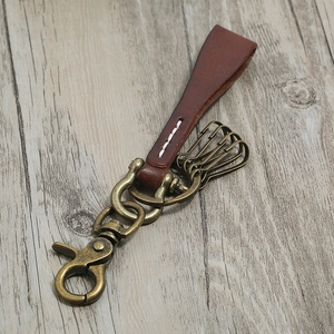 Vintage brown leather keychain with brass alloy hardware on light wood background