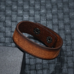 Vintage brown leather cuff bracelet for men with dual metal button snaps on dark background