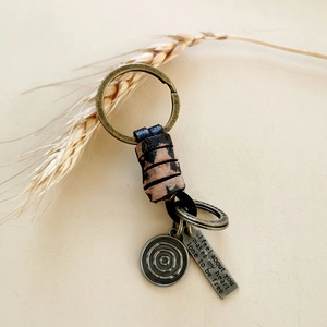 Detail of vintage braided leather keychain with engraved bronze motivational tag and charm