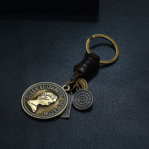 Vintage bronze Elizabeth II coin keychain with dark brown woven leather on black texture