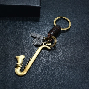 Vintage bronze saxophone keychain with woven leather strap on premium black background