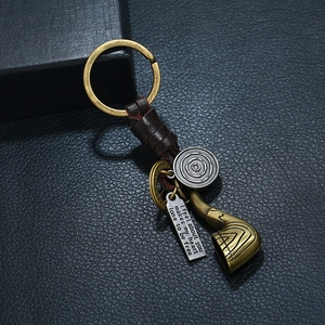 Vintage braided leather keychain with brass pipe charm and engraved quote tag on grey texture
