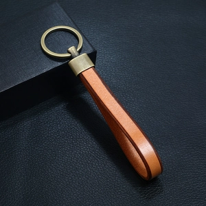 Close-up of vintage brown leather keychain with brass metal ring on black leather background