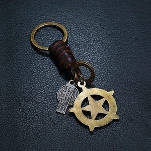 Vintage braided leather keychain with star pendant and bronze charms on black background