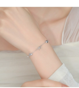 Détail du bracelet en argent 925 avec breloques lapin, nœud et cœur au poignet de femme