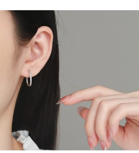 Dettaglio di orecchini a cerchio in argento 925 con zirconi su una modella donna