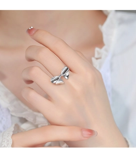 Detail view of a silver bow knot ring on finger showing delicate metal texture