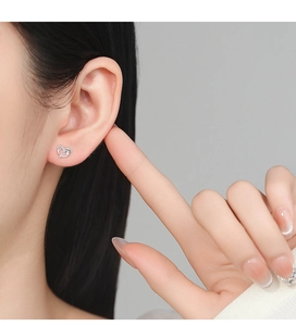 Close-up of heart-shaped hollow silver earrings on ear with elegant metallic finish