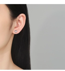 Close-up of heart-shaped 925 silver stud earring with glowing blue moonstone on ear
